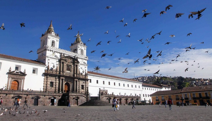 Iglesia de San Francisco de Quito con el museo Fray Pedro Gocial, la plaza y palomas volando sobre ella, cielo azul