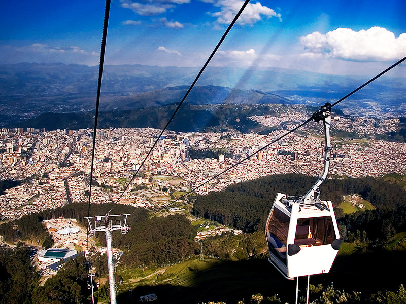 Cabinas del teleférico en el aire, con la ciudad de Quito de fondo